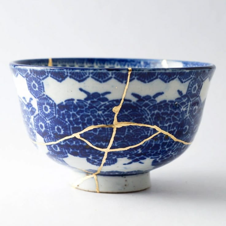 A blue-and-white porcelain bowl repaired with kintsugi, its cracks filled with visible gold seams.